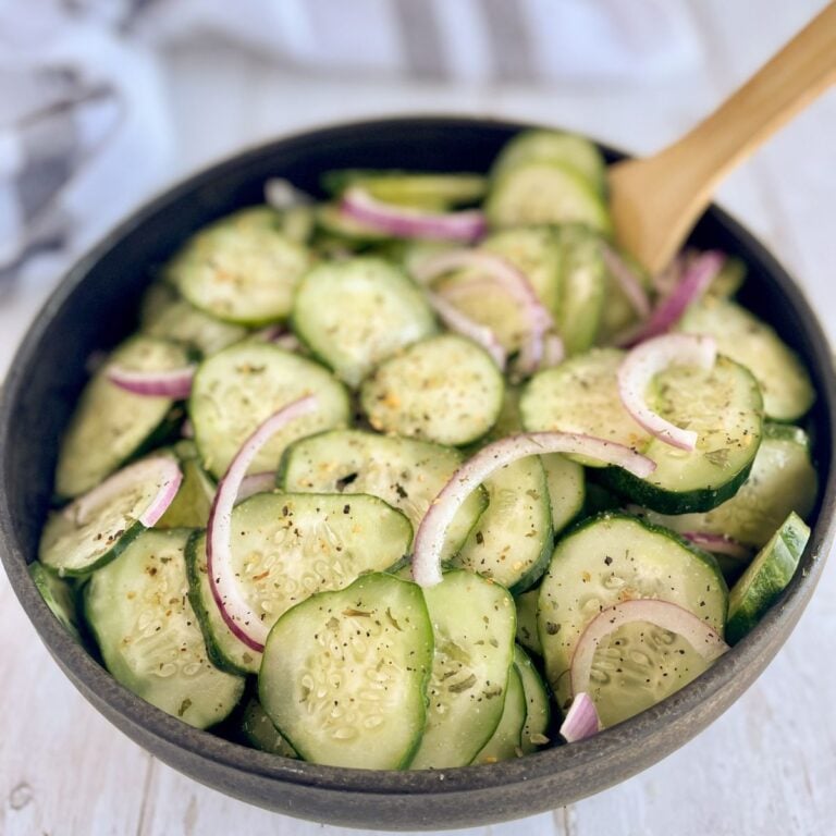 A close-up of keto cucumber onion salad in a black bowl, showing crisp cucumber slices, thinly sliced red onions, and a tangy vinegar dressing.