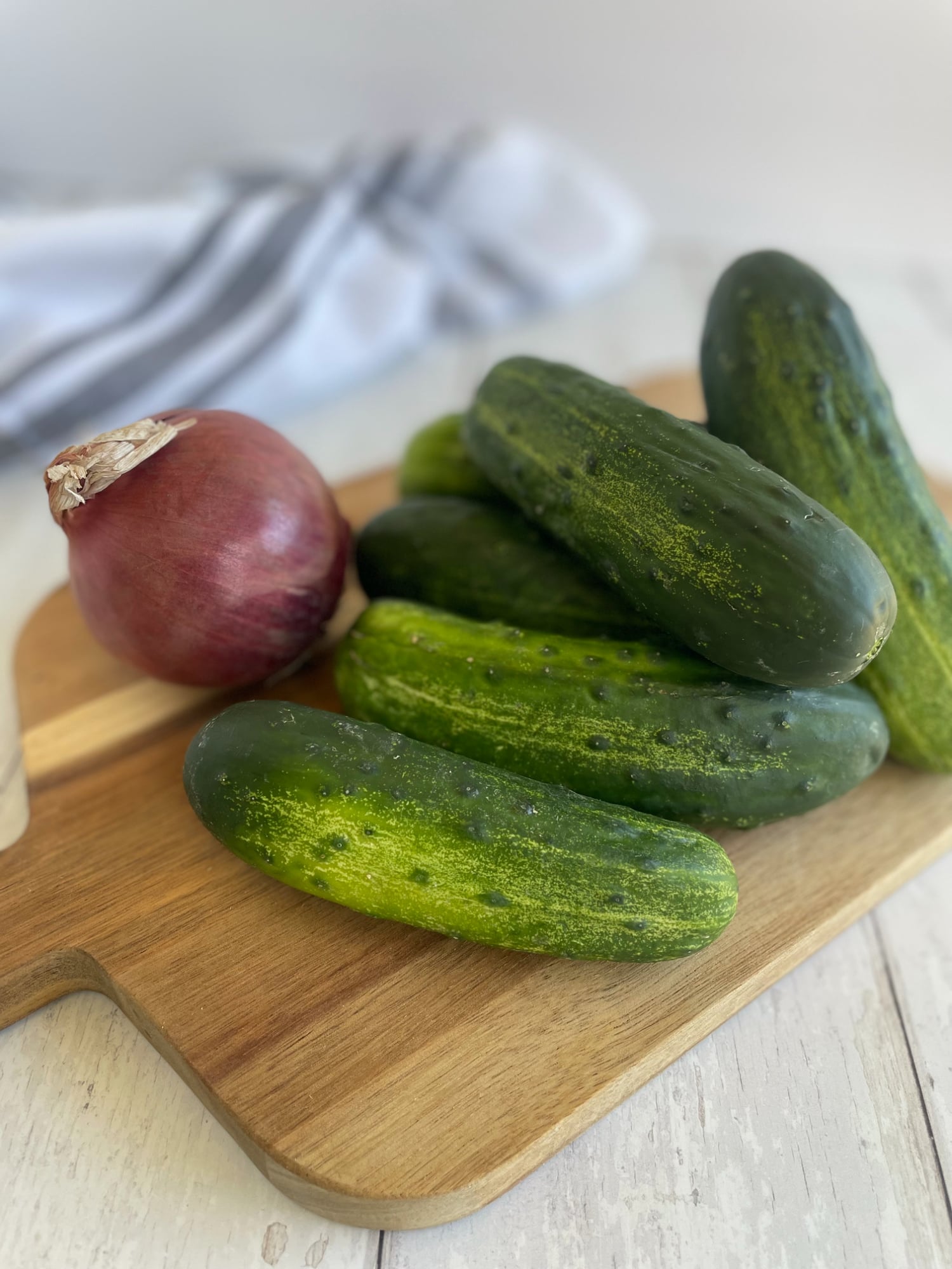 Whole pickling cucumbers and a red onion resting on a wooden cutting board, ready to be sliced for a keto cucumber onion salad.
