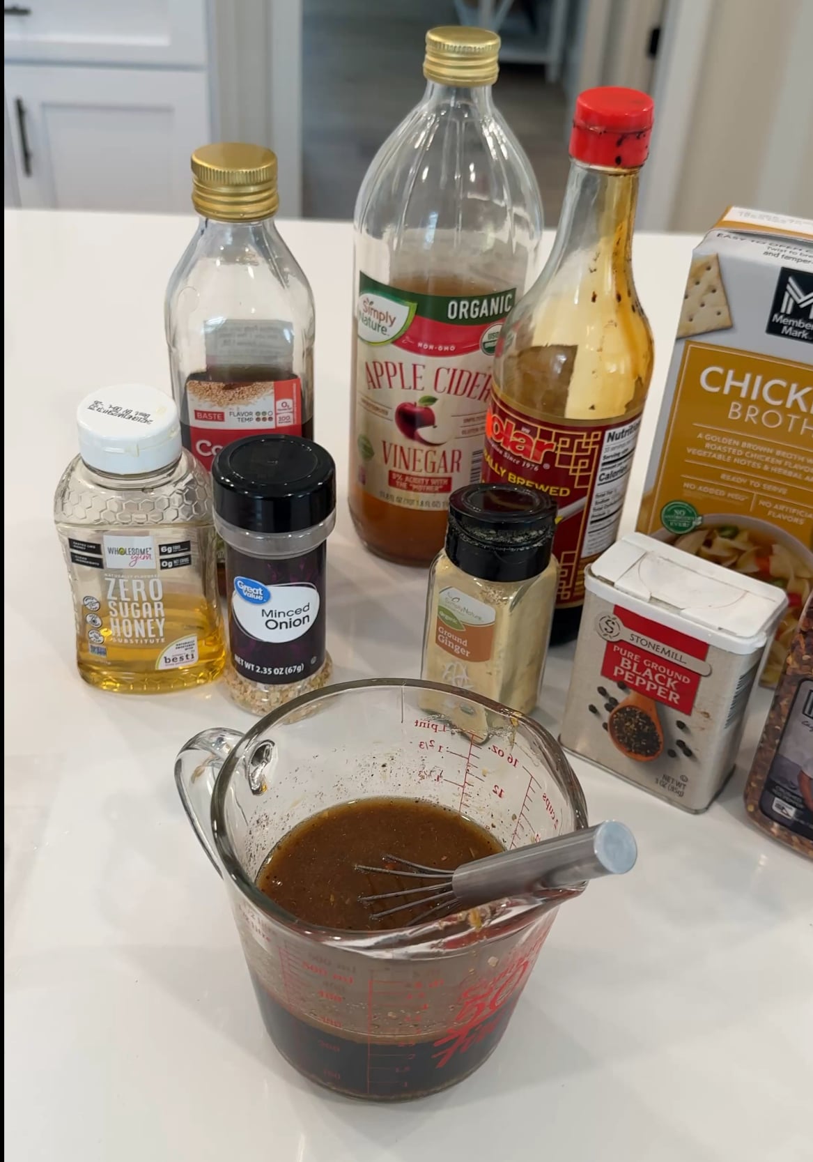 Ingredients for keto honey garlic chicken including soy sauce, apple cider vinegar, low-carb honey substitute, minced onion, and chicken broth with a measuring cup of mixed sauce.