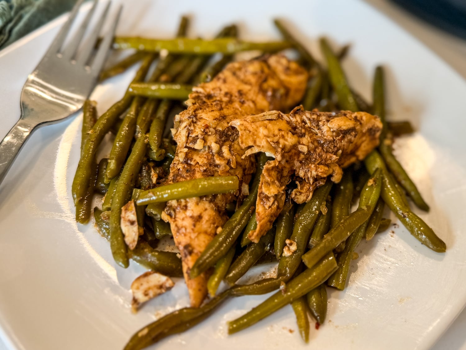 Keto honey garlic chicken tenders and green beans served on a white plate with a fork.