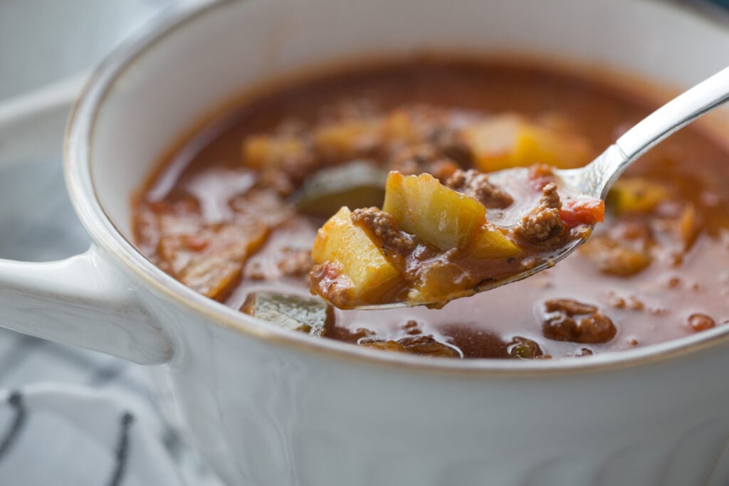 White bowl of keto vegetable soup with ground beef, vegetables, and a spoonful ready to eat
