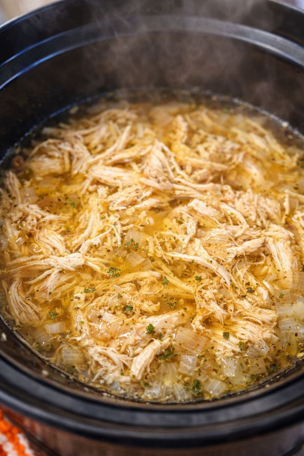 Shredded chicken cooking in a slow cooker with broth and onions for healthy Tuscan chicken soup