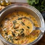 Creamy Tuscan chicken soup with spinach and sun-dried tomatoes in a stainless steel pot with a ladle